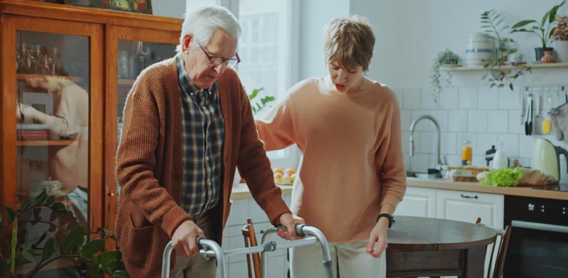 Persona mayor con andador acompañada de una persona que le apoya